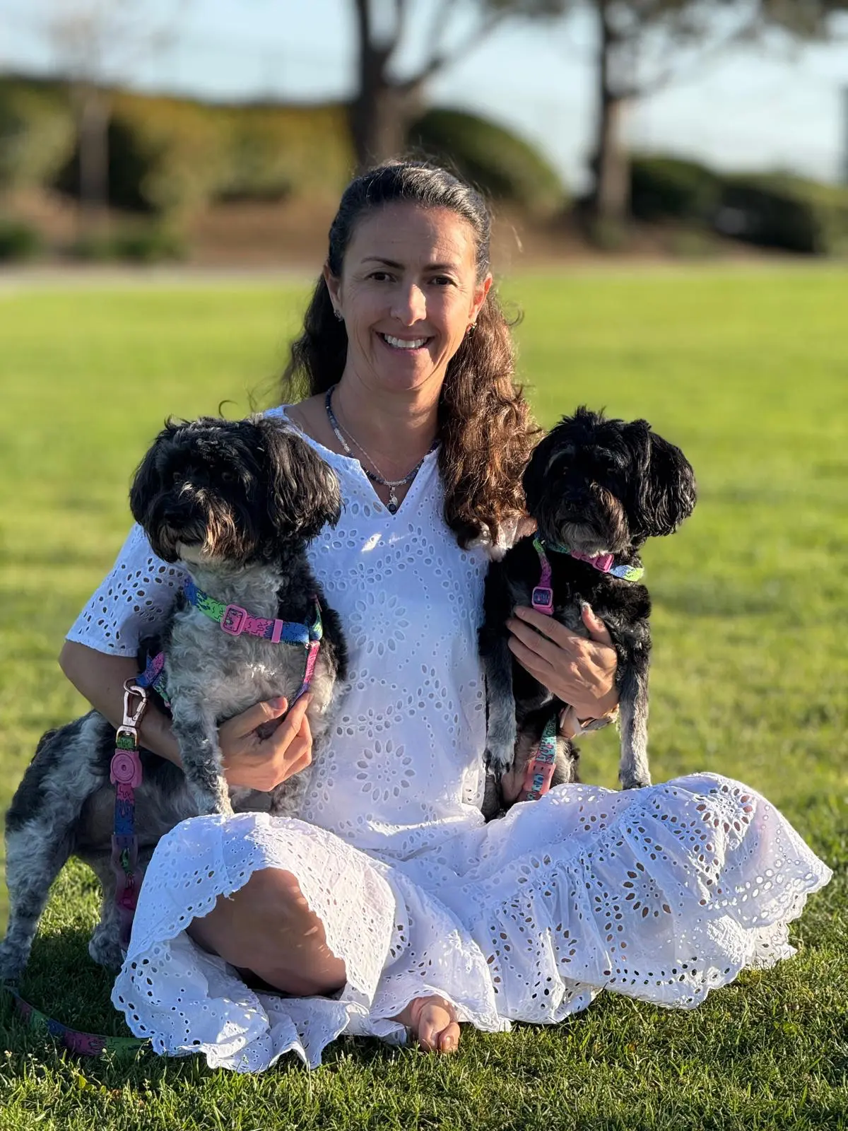 Daiana sitting on the grass and smiling while holding her two dogs